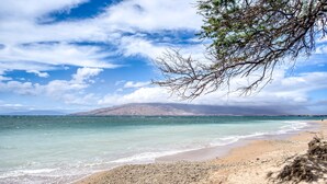 A beach with clear turquoise water, a sandy shore, and a distant mountain.