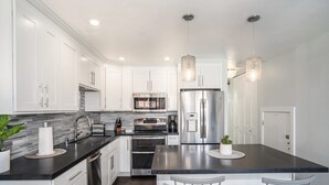 A modern kitchen with white cabinets, stainless steel appliances, a black countertop, and two pendant lights.
