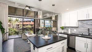 A modern kitchen with a large island, white cabinetry, and a view of a balcony with outdoor furniture.