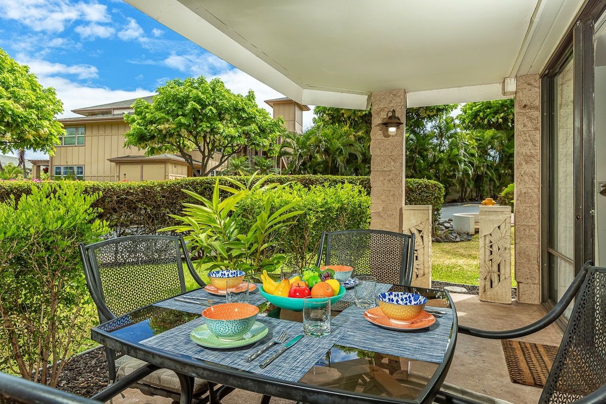 An outdoor dining area with a table set for four, surrounded by greenery and a view of neighboring houses.