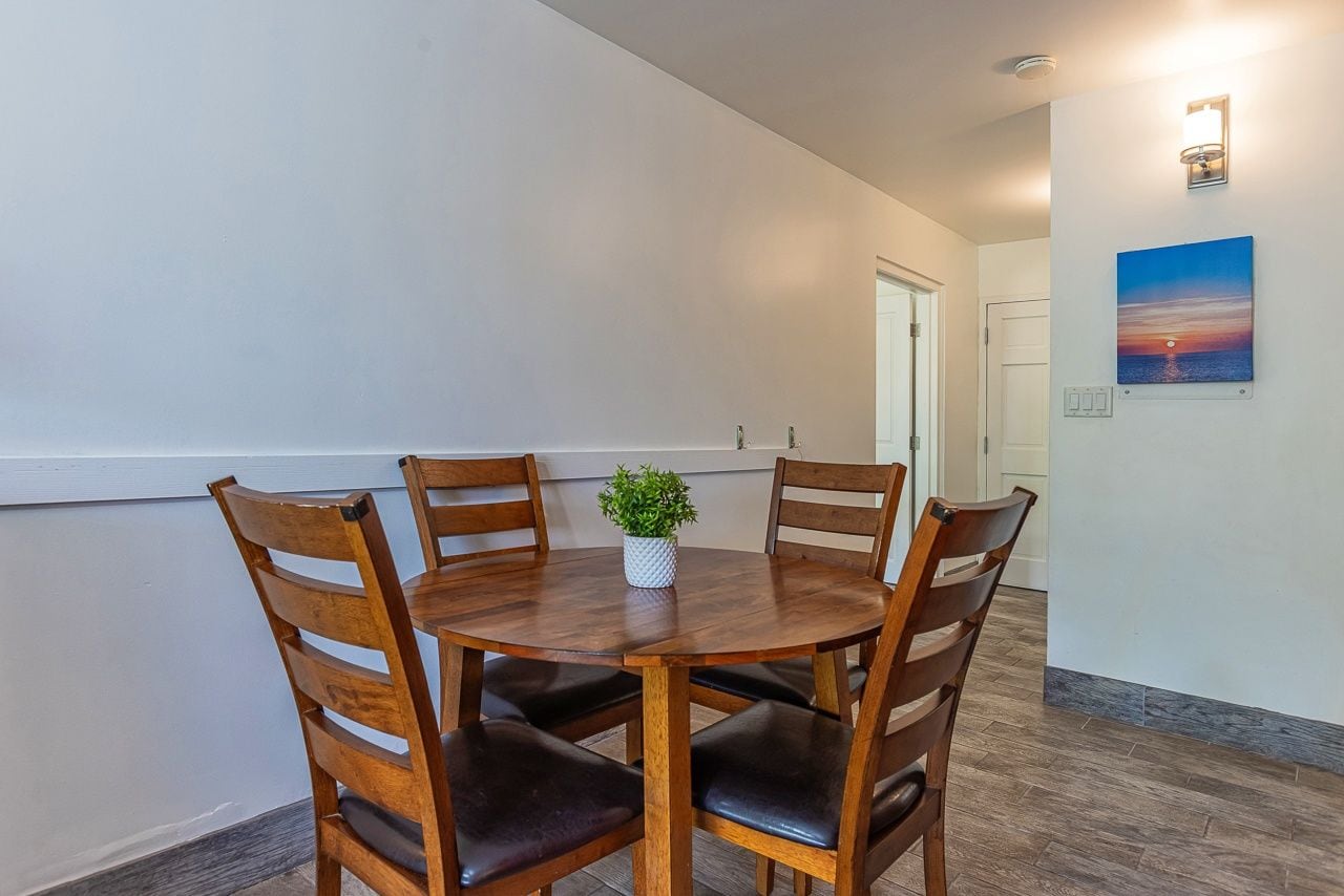 A dining area with a round wooden table, four chairs, and a small potted plant.