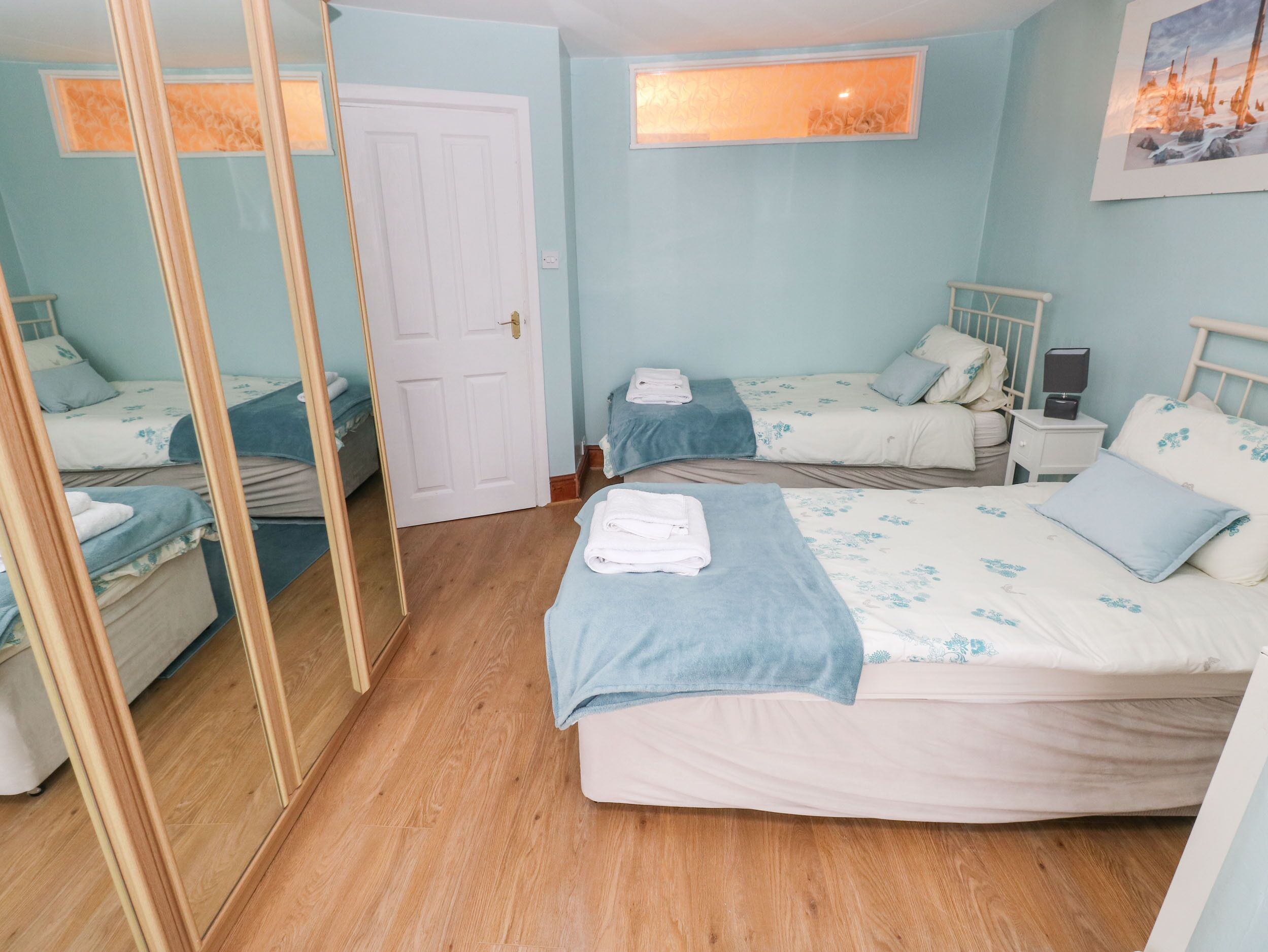 Une chambre avec deux lits, un miroir, une porte et une table de chevet avec une lampe.