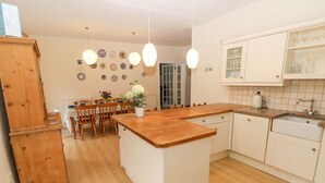 A kitchen with wooden cabinets, a central island, and a dining area with chairs and a table. - Gower View (Tenby)