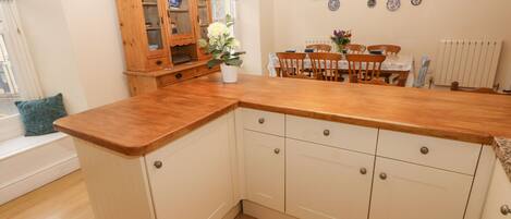 A kitchen with wooden cabinets, a wooden countertop, and a dining area with a table and chairs.