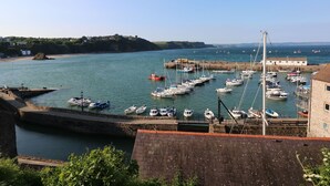 A harbor with numerous boats docked, a lighthouse, and a building with a red roof. - Gower View (Tenby)