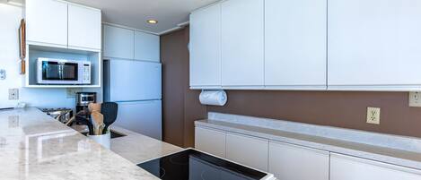 A modern kitchen with white cabinets, a built-in microwave, a stainless steel refrigerator, and a countertop with a built-in induction cooktop.