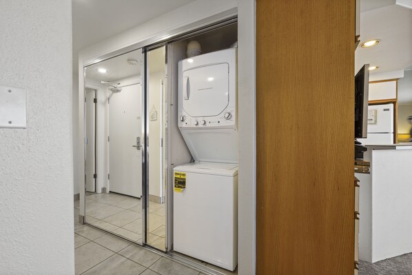 A laundry room with a front-loading washer and dryer, a wooden door, and a tiled floor.