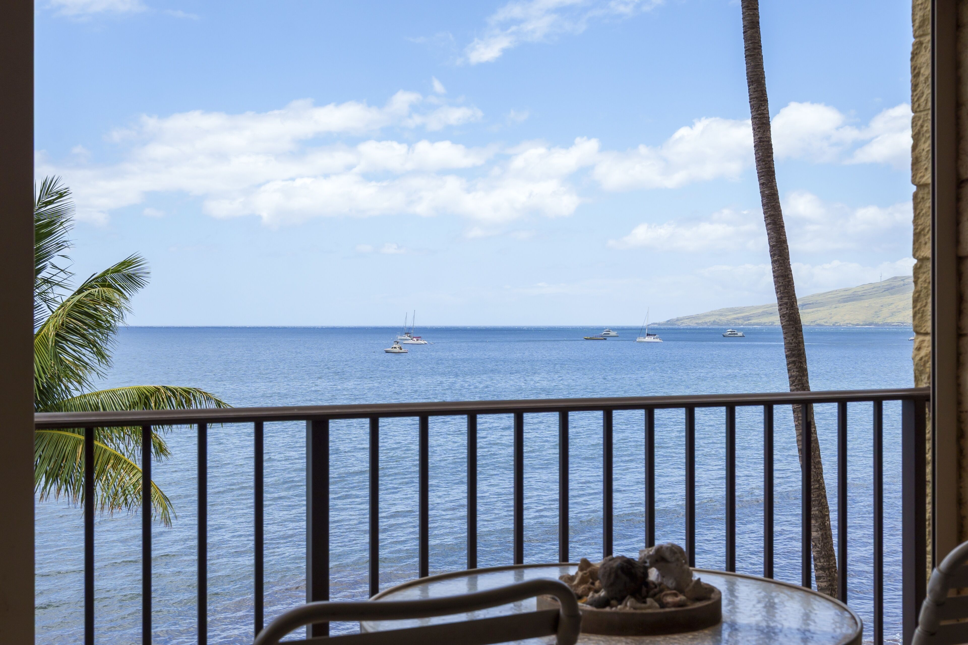 Ein Balkon mit Blick auf das Meer, Palmen und einem Tisch mit einer Skulptur.