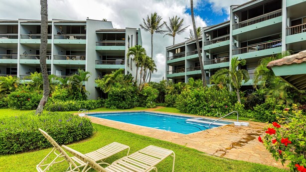 Un hotel con piscina, sillones de descanso y abundante vegetación.