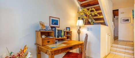 Un bureau en bois, une chaise rouge, une lampe et une bibliothèque remplie de livres et de photos encadrées.