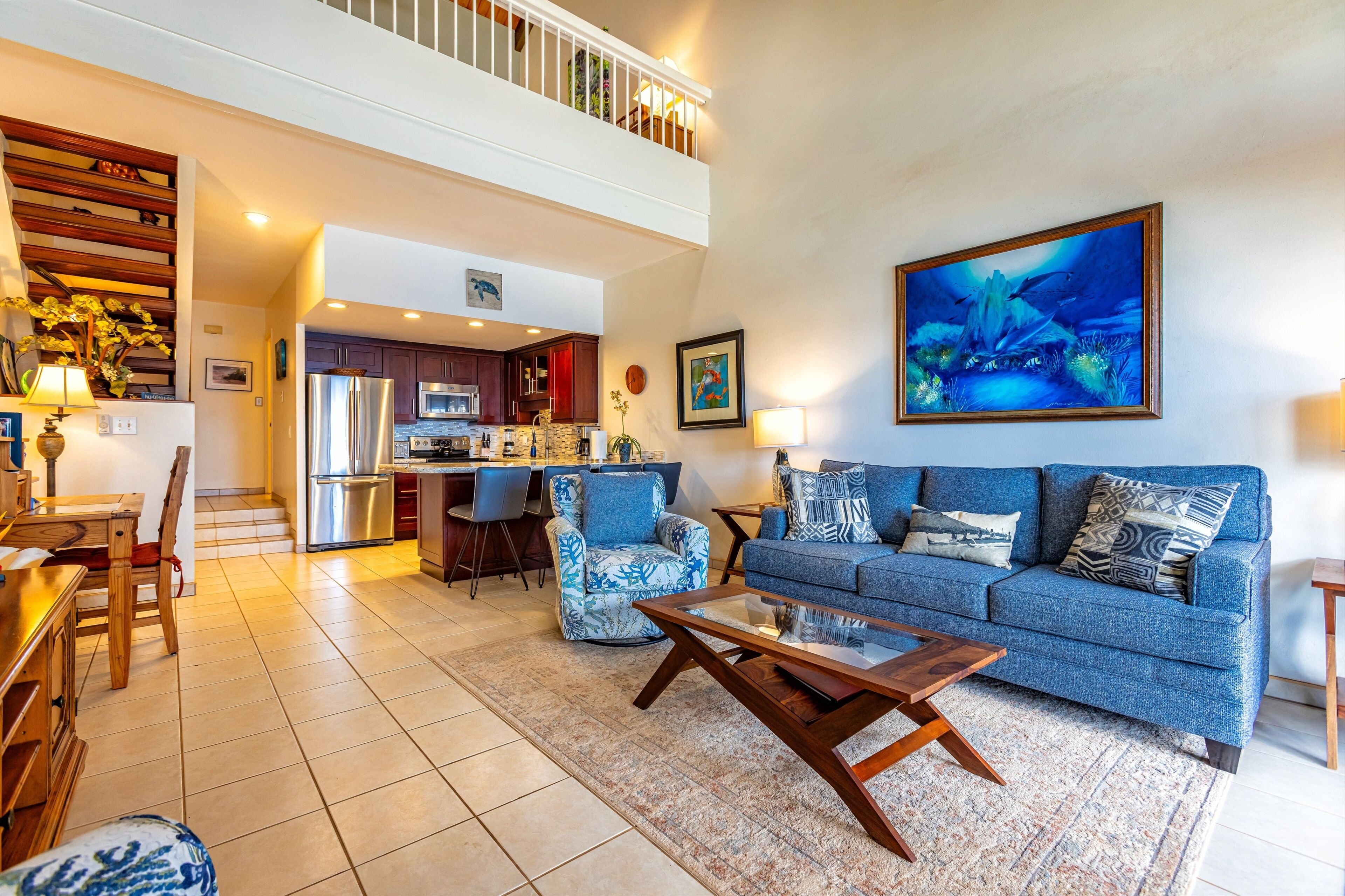 A spacious living area with a blue sofa, a coffee table, and a kitchen in the background.