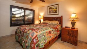 A bedroom with a bed, two bedside lamps, a ceiling fan, a window with blinds, and a painting on the wall.