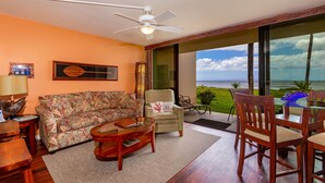Sala de estar com vista para o oceano, ventoinha no teto e sofá com estampa tropical.