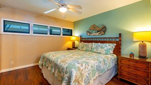 Quarto com cama, mesa de cabeceira, abajur, ventilador de teto e uma obra de arte pendurada na parede.