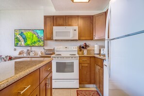 A kitchen with wooden cabinets, a microwave, a stove, and a refrigerator. - Kihei Surfside, #109 1 Bedroom Condo by RedAwning (Kihei)