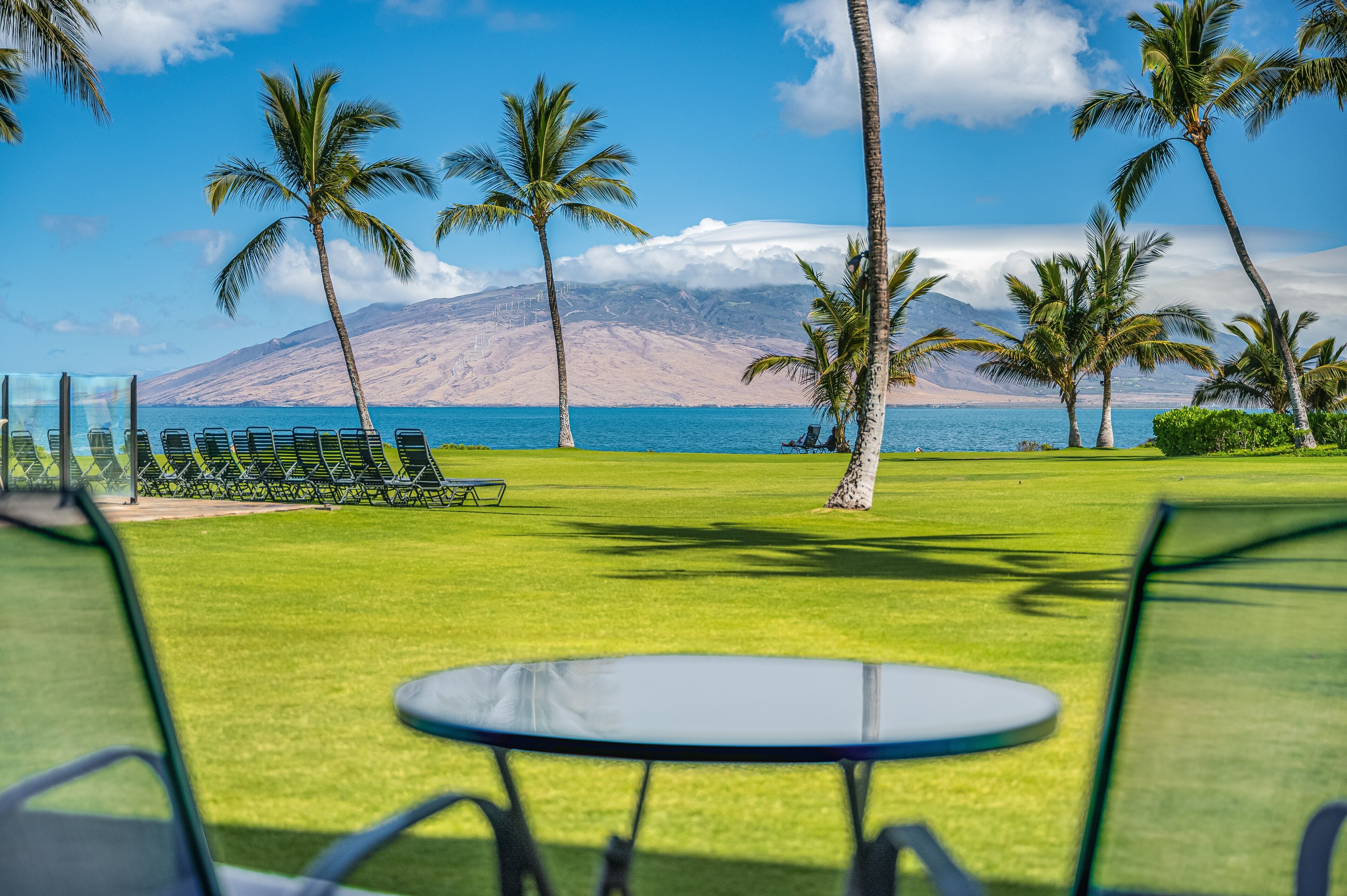 A view of a golf course with a table and chairs in the foreground, palm trees, and a mountain in the background.