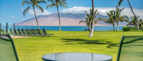 A view of a golf course with a table and chairs in the foreground, palm trees, and a mountain in the background.