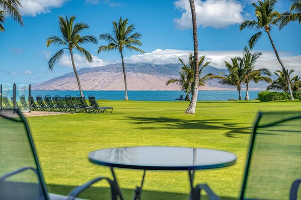 A view of a golf course with a table and chairs in the foreground, palm trees, and a mountain in the background.