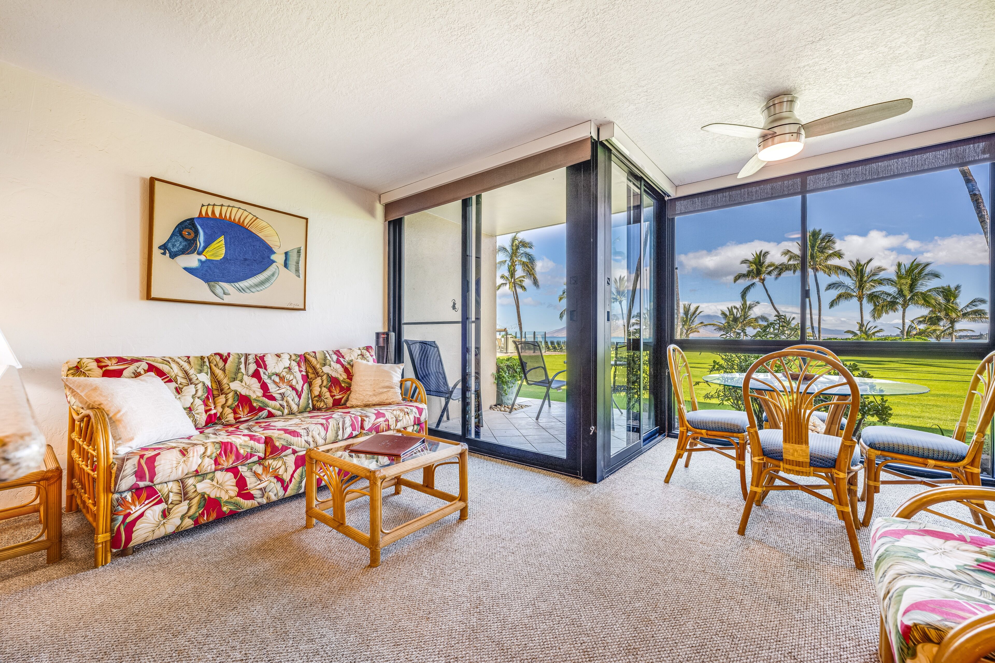 A room with a sofa, chairs, a table, and a large window with a view of palm trees.