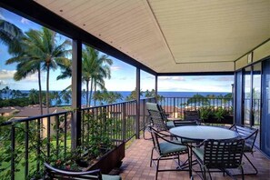 A covered outdoor area with a table and chairs, overlooking a beach with palm trees. - Wailea Elua, #2010 2 Bedroom Condo by RedAwning (Kihei)