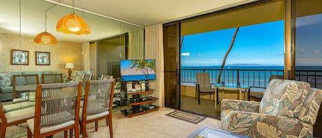 A hotel room with a balcony, a television, a sofa, and a dining area.