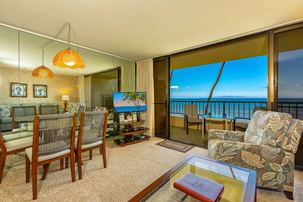 Habitación de hotel con balcón, televisión, sofá y zona de comedor.