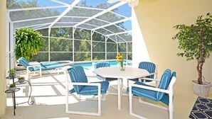 A covered outdoor area with a pool, lounge chairs, and a table.