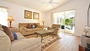 A living room with a sofa set, coffee table, and lamps. There are two framed pictures on the wall and a ceiling fan.