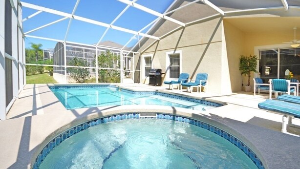 A covered outdoor swimming pool with blue chairs and a barbecue grill.