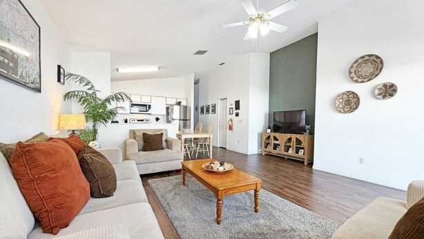 A living room with a sofa, coffee table, and a TV stand. There is a ceiling fan and a kitchen area in the background. - Bloomingdale Villa 4 Bedroom Home by RedAwning (Davenport)