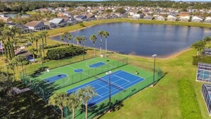 An aerial view of a residential area with a tennis court, a lake, and houses. - Bloomingdale Villa 4 Bedroom Home by RedAwning (Davenport)