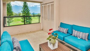 A balcony with a view of a golf course, a blue sofa set, and a wooden table with a plant. - Big Island Waikoloa Fairways by Coldwell Banker Island Vacations (Waikoloa)