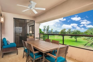 A balcony with a wooden table and chairs, a ceiling fan, and a view of a green landscape.