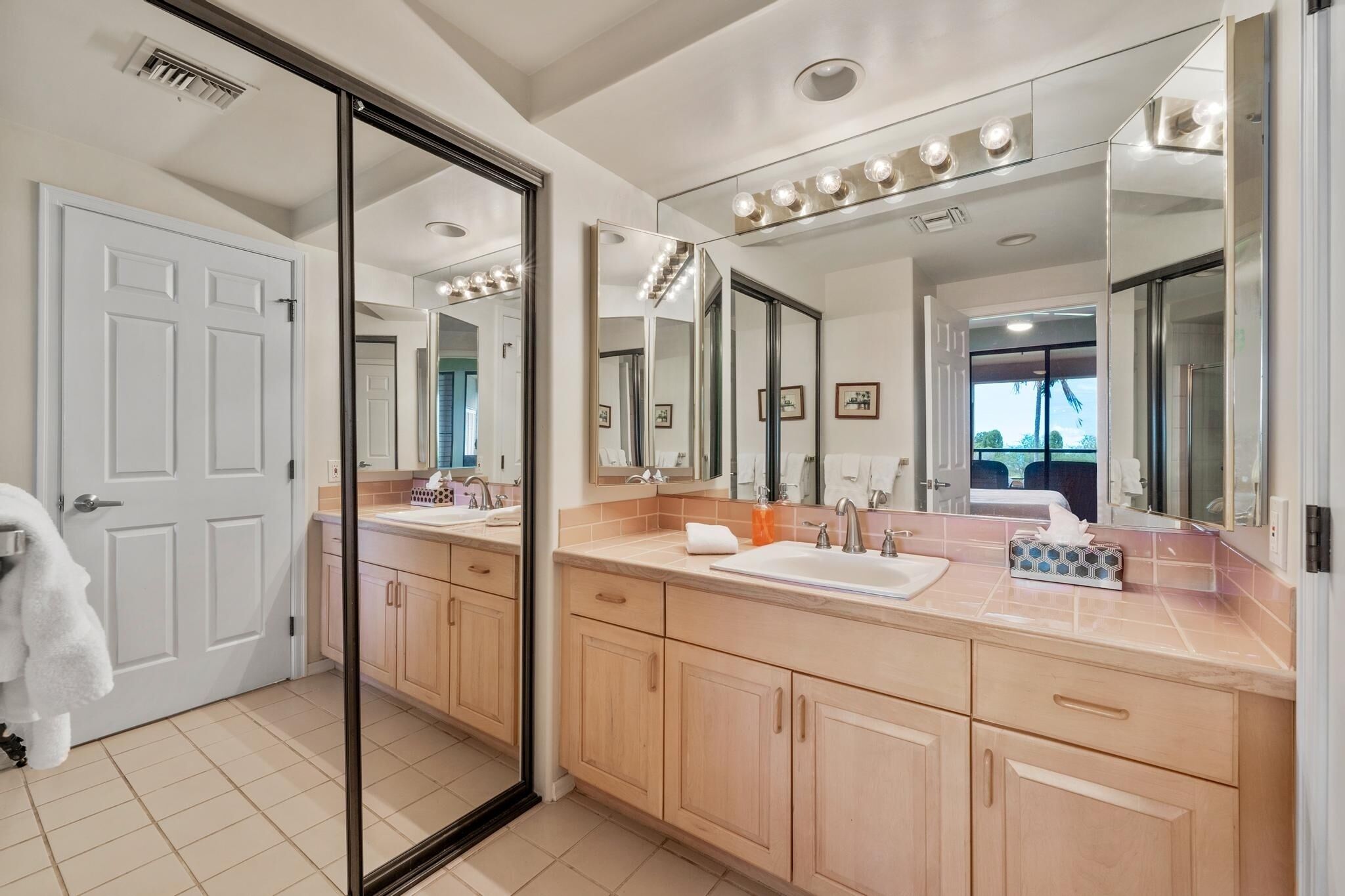 A modern bathroom with two sinks, a large mirror, and a sliding glass door leading to a balcony.