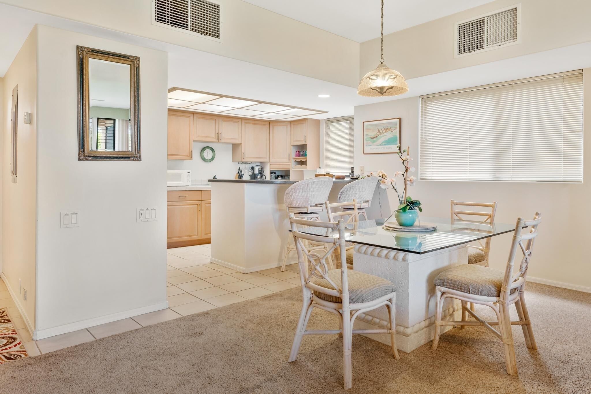 A modern kitchen with white cabinets, a central island, and a dining area with a glass table and wicker chairs.