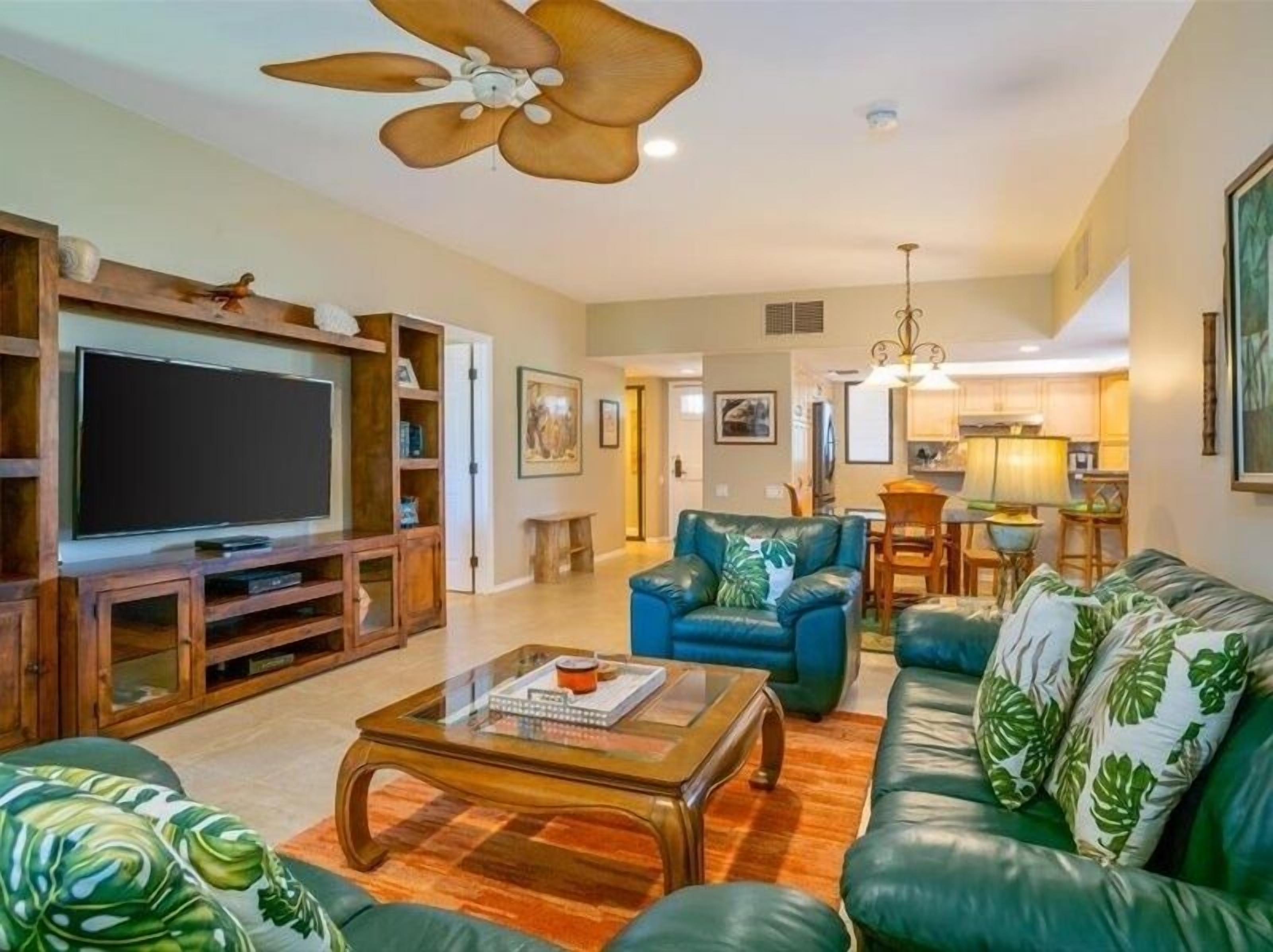 A living room with a television, leather sofas, a coffee table, and a ceiling fan.