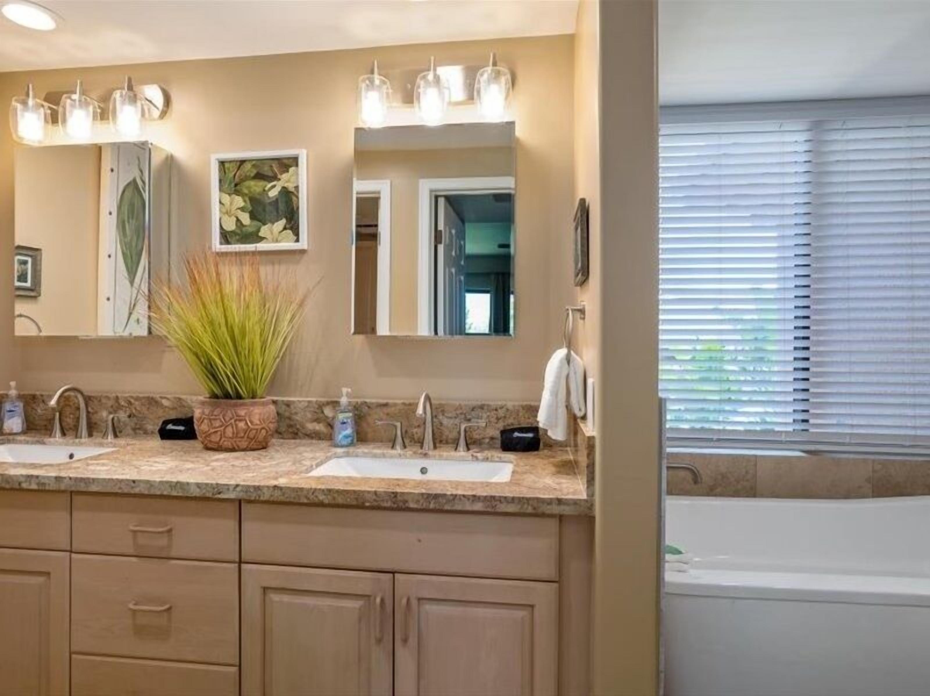 A bathroom with a double sink, a potted plant, a mirror, and a bathtub.