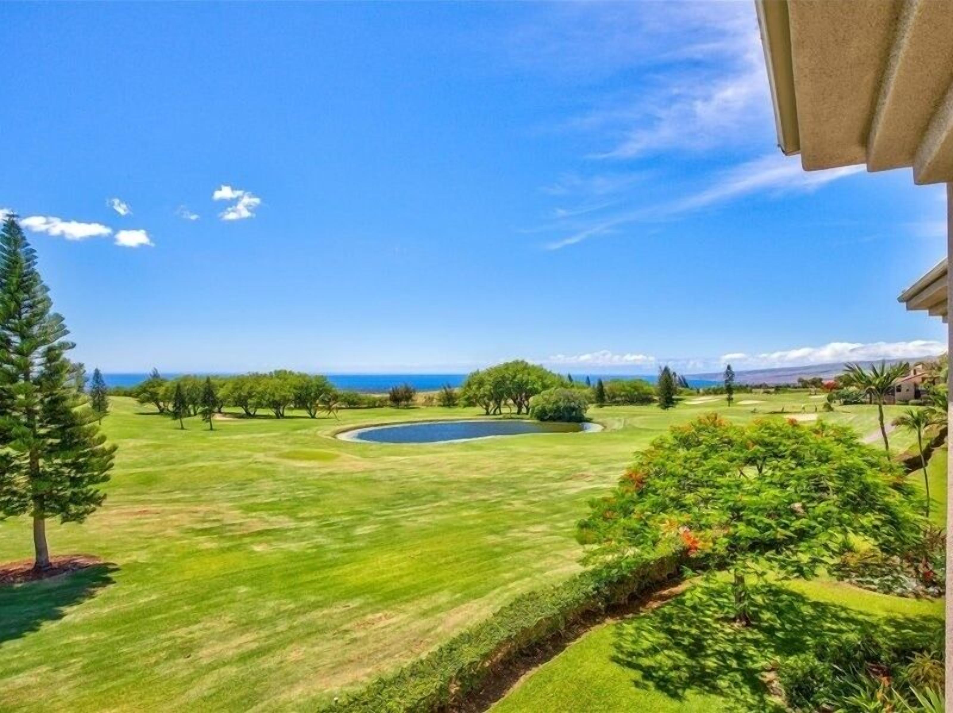 A golf course with a pond, trees, and a view of the ocean.