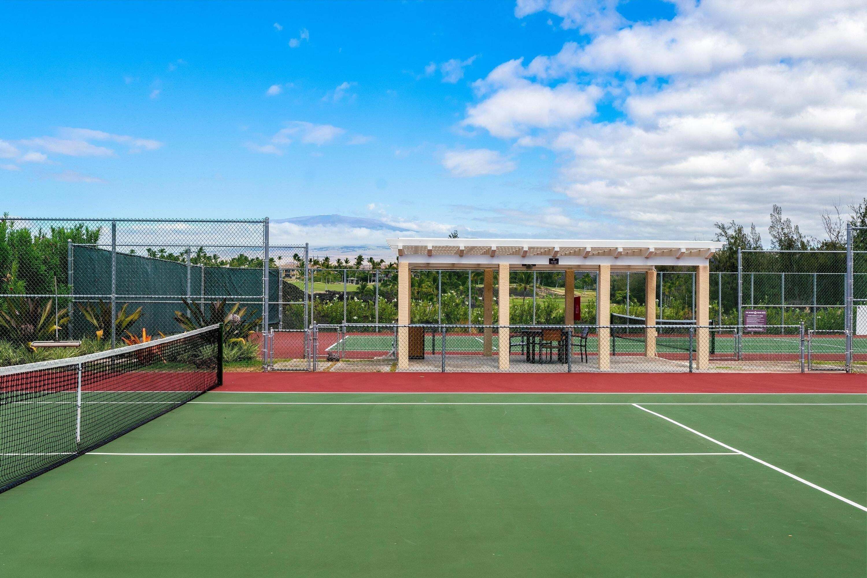Una cancha de tenis con una red, un área de estar techada y una valla.