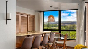 Une cuisine moderne avec un coin bar, des volets en bois et une grande fenêtre donnant sur un paysage verdoyant.