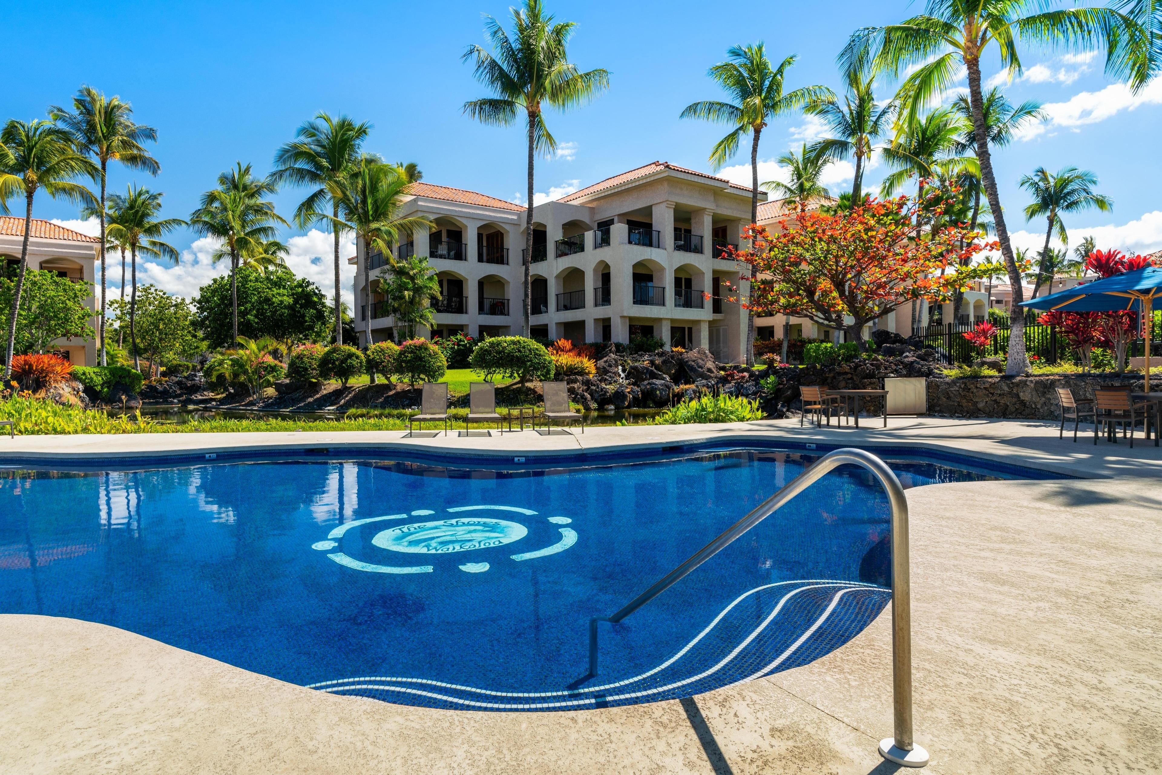 A swimming pool with a lifeguard stand, surrounded by palm trees and lounge chairs.