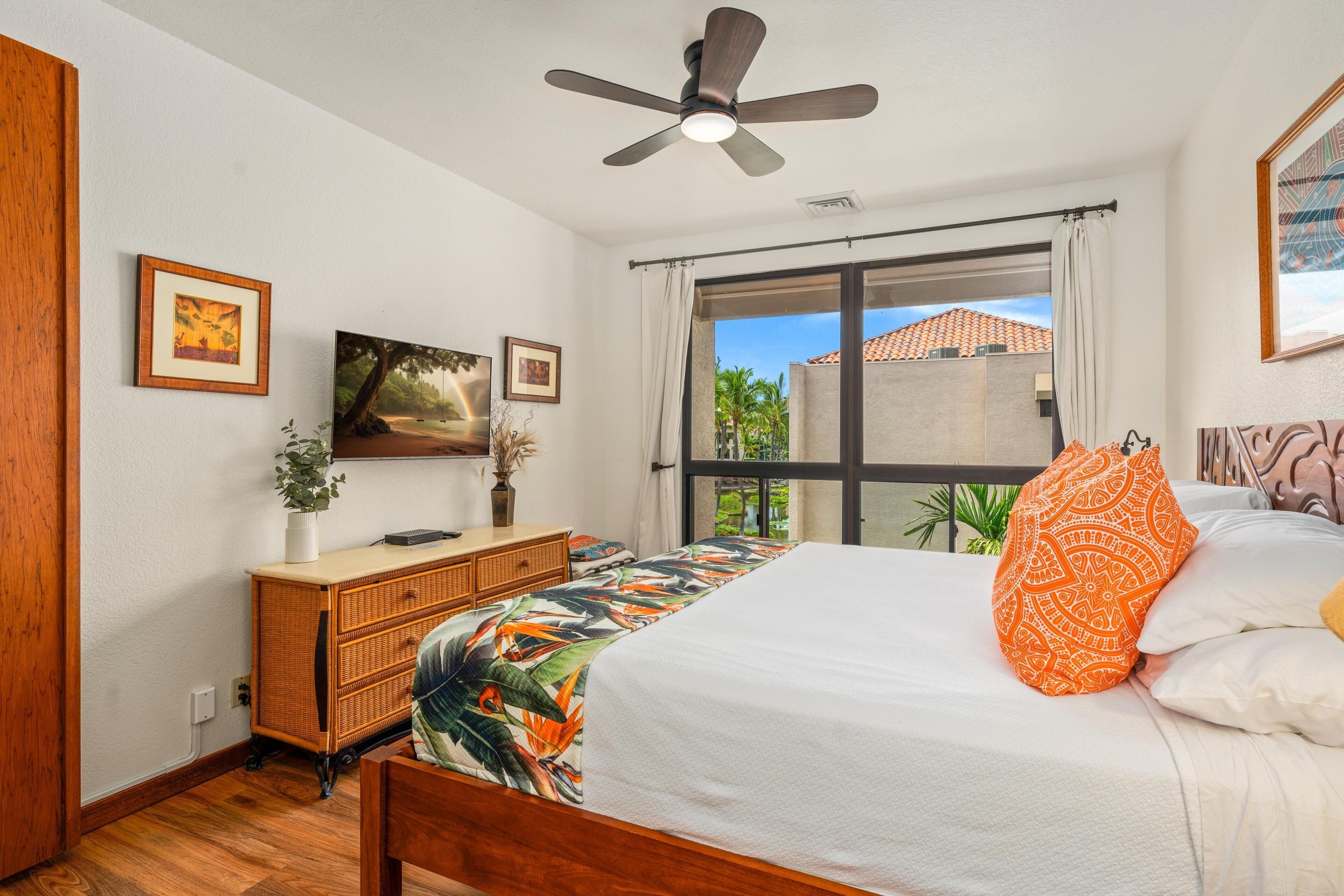 A bedroom with a bed, a ceiling fan, a window with curtains, a dresser, and framed pictures on the wall.