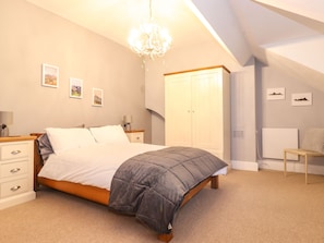 Une chambre à coucher comprenant un lit, des tables de chevet, une armoire, un radiateur et un lustre.