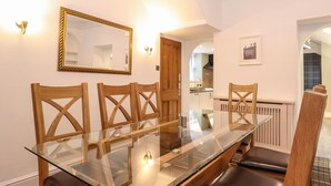 Un comedor con una mesa de vidrio y sillas de madera, un espejo en la pared, y una cocina visible a través de una puerta abierta.