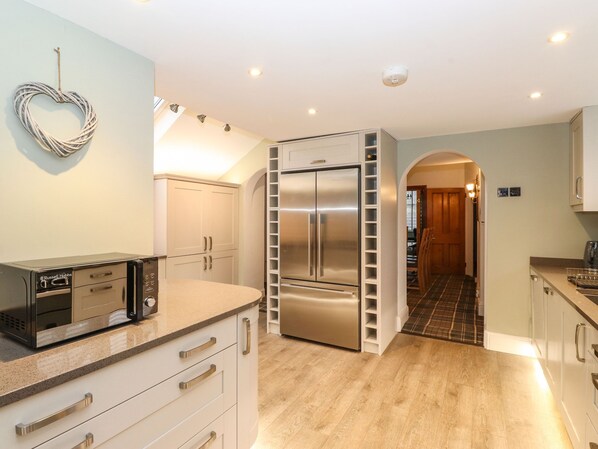 A modern kitchen with a built-in refrigerator, microwave, and oven. There is a heart-shaped decoration on the wall and a wooden floor.