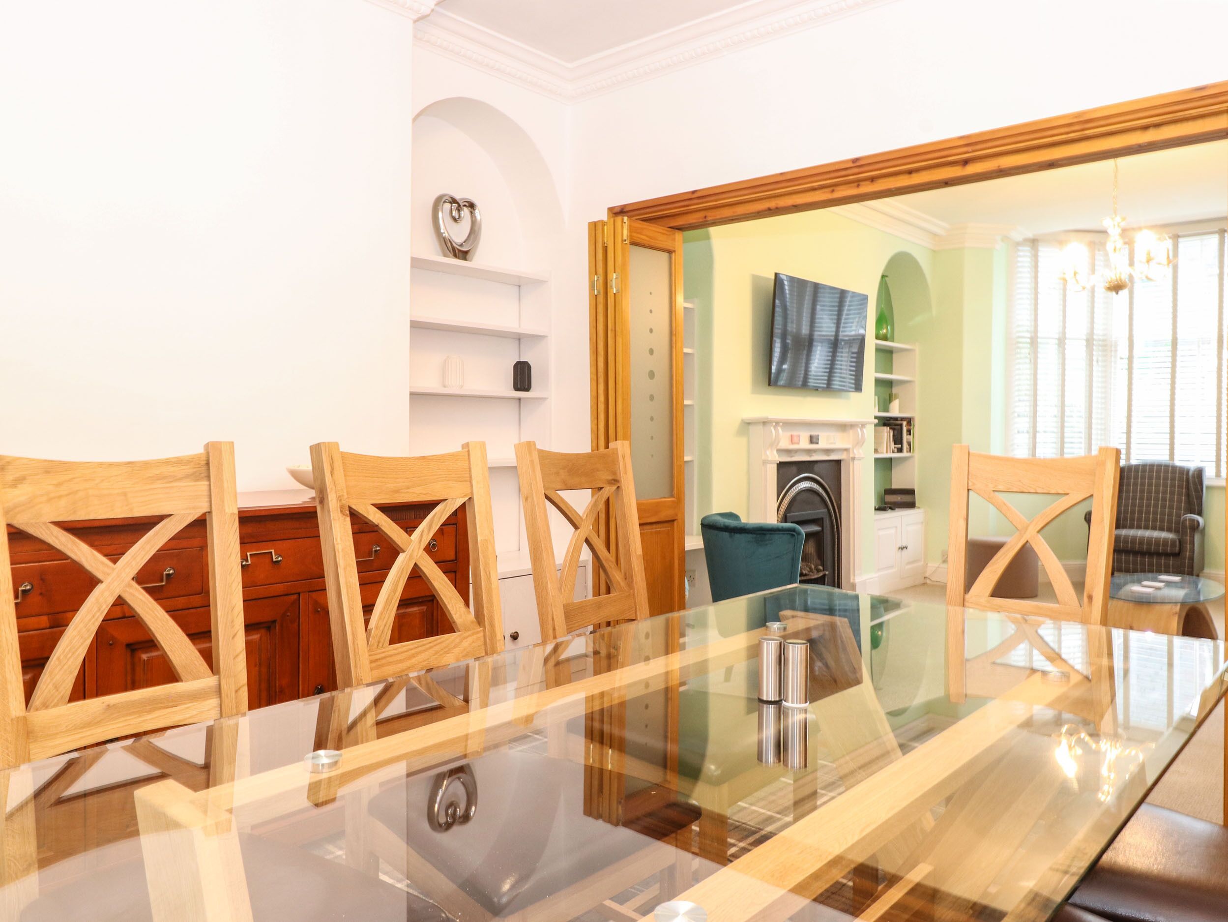A dining area with a glass-top table and wooden chairs, a fireplace, and a television mounted on the wall.