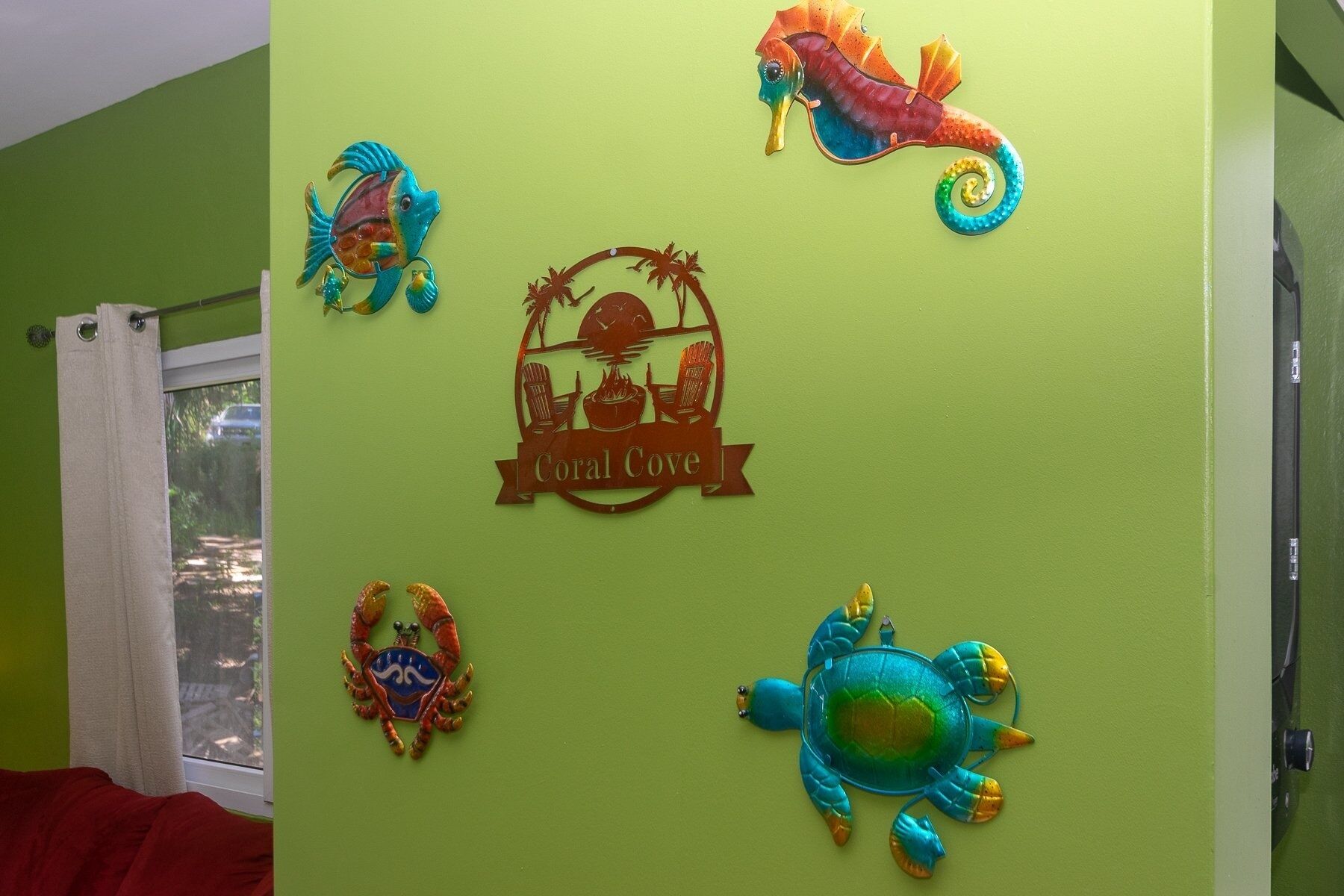 A room with a green wall decorated with various sea creature ornaments, a window with a white curtain, and a red bedspread.
