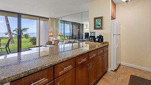 A kitchen with a large island, wooden cabinets, a refrigerator, and a view of the ocean. - Sugar Beach Resort, #130 1 Bedroom Condo by RedAwning (Kihei)
