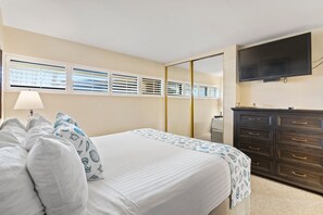 Una habitación de hotel con cama, cómoda, televisor y ventana con persianas.
