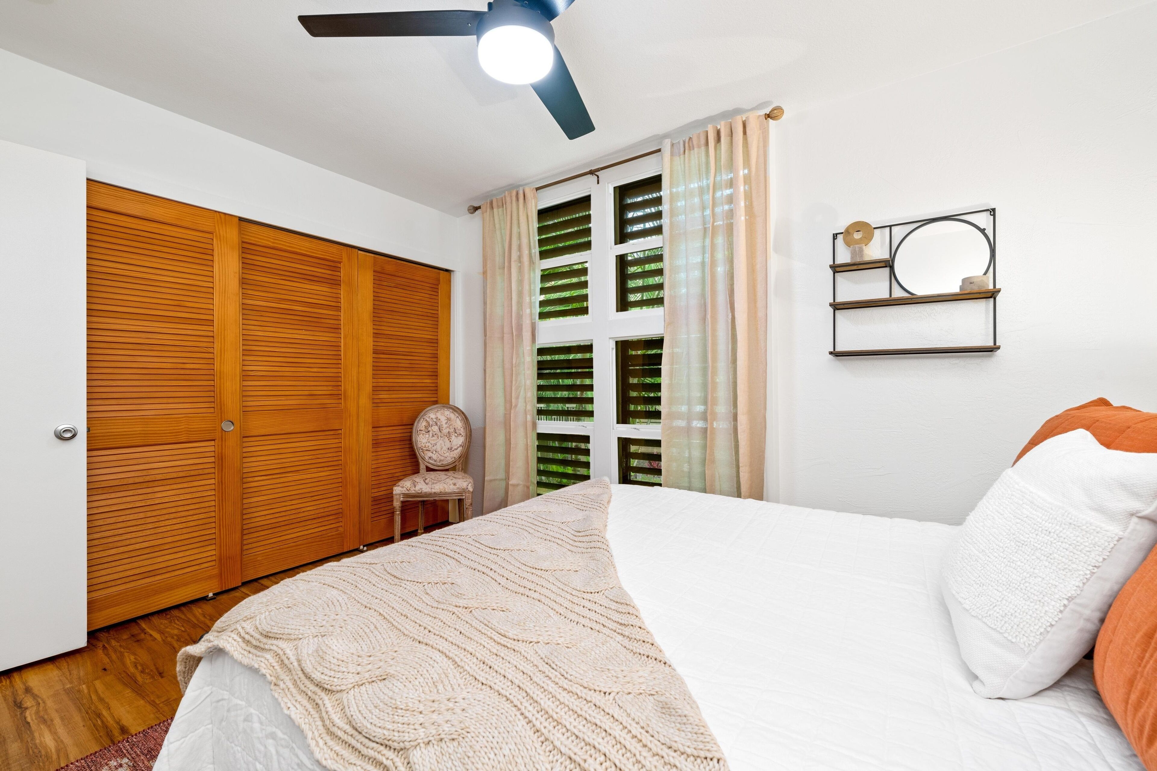 A bedroom with a bed, a ceiling fan, a wardrobe, and a window with curtains.